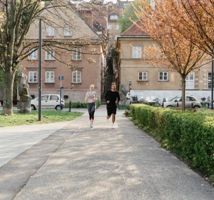 A couple jogging together in an urban park surrounded by greenery and houses.